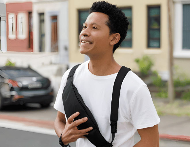 A man in casual attire strolls confidently with a chest bag across his chest, the bag's sleek black fabric contrasting against the man's white t-shirt.